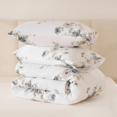 Stack of two floral pillows and a folded comforter on a white fitted sheet.