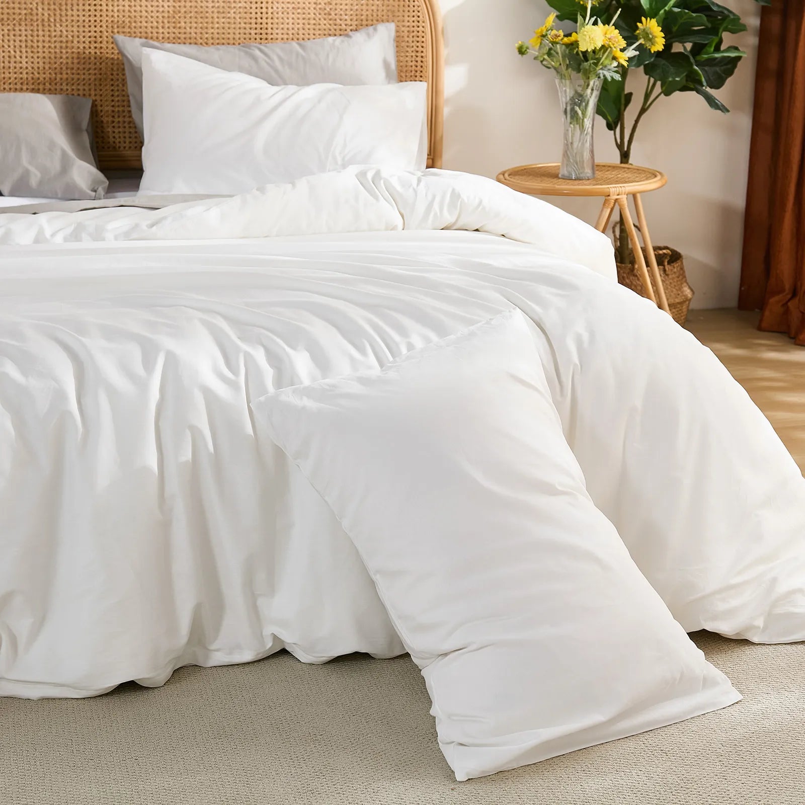 Angled view from the front left showing the white duvet fully spread on the bed, accented by sunflowers on the side table.
