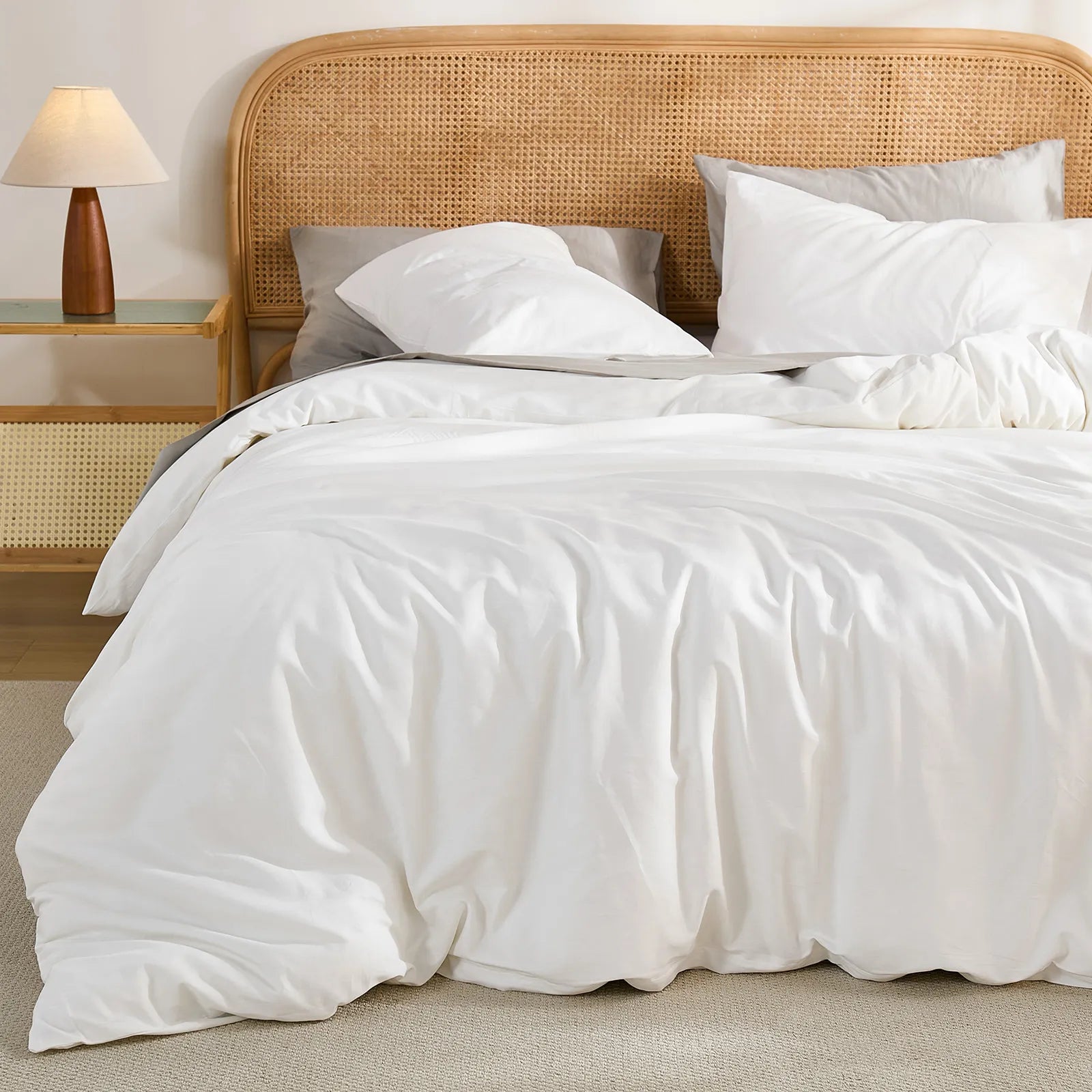 Close-up detail shot of the white duvet and layered pillows, highlighting the woven texture of the rattan headboard.
