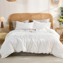 Straight-on front view of a white solid cotton duvet on a bed with a rattan headboard, side tables with lamp and yellow flowers.