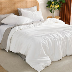 View from the right side of the bed showing the white duvet, a round rattan table with a vase of yellow flowers, and soft natural light.