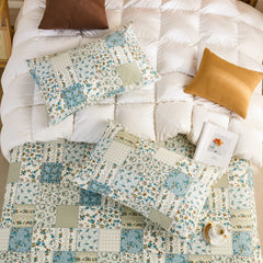 Overhead shot of two cotton patchwork pillowcases and a matching sheet set on a white quilted duvet.