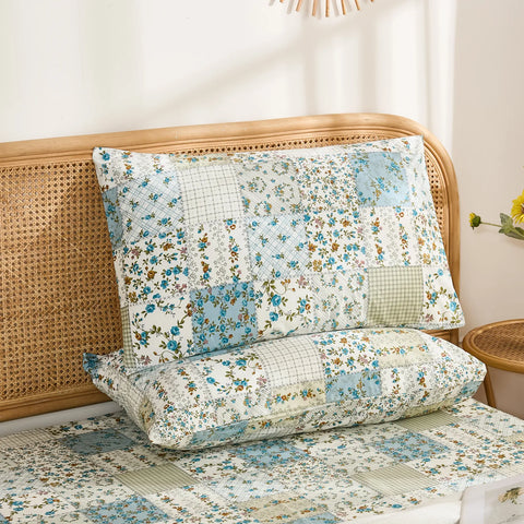 A pair of cotton pillowcases featuring a blue floral and plaid patchwork print, stacked against a rattan headboard.