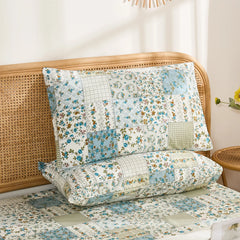 A pair of cotton pillowcases featuring a blue floral and plaid patchwork print, stacked against a rattan headboard.