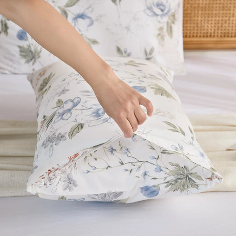 A hand adjusting the pillow in the cotton pillowcase, showing the envelope closure detail and the light blue floral print.