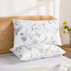 Two cotton pillowcases featuring a delicate blue and white floral sketch design, stacked on a bright bed setup.