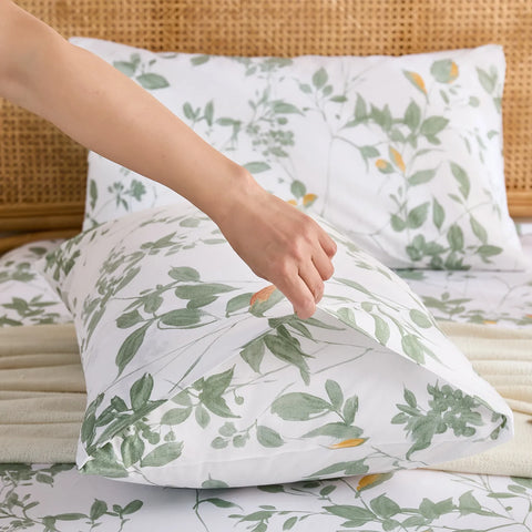 A hand adjusting the pillow in the cotton pillowcase, showing the envelope closure detail and green leafy pattern.