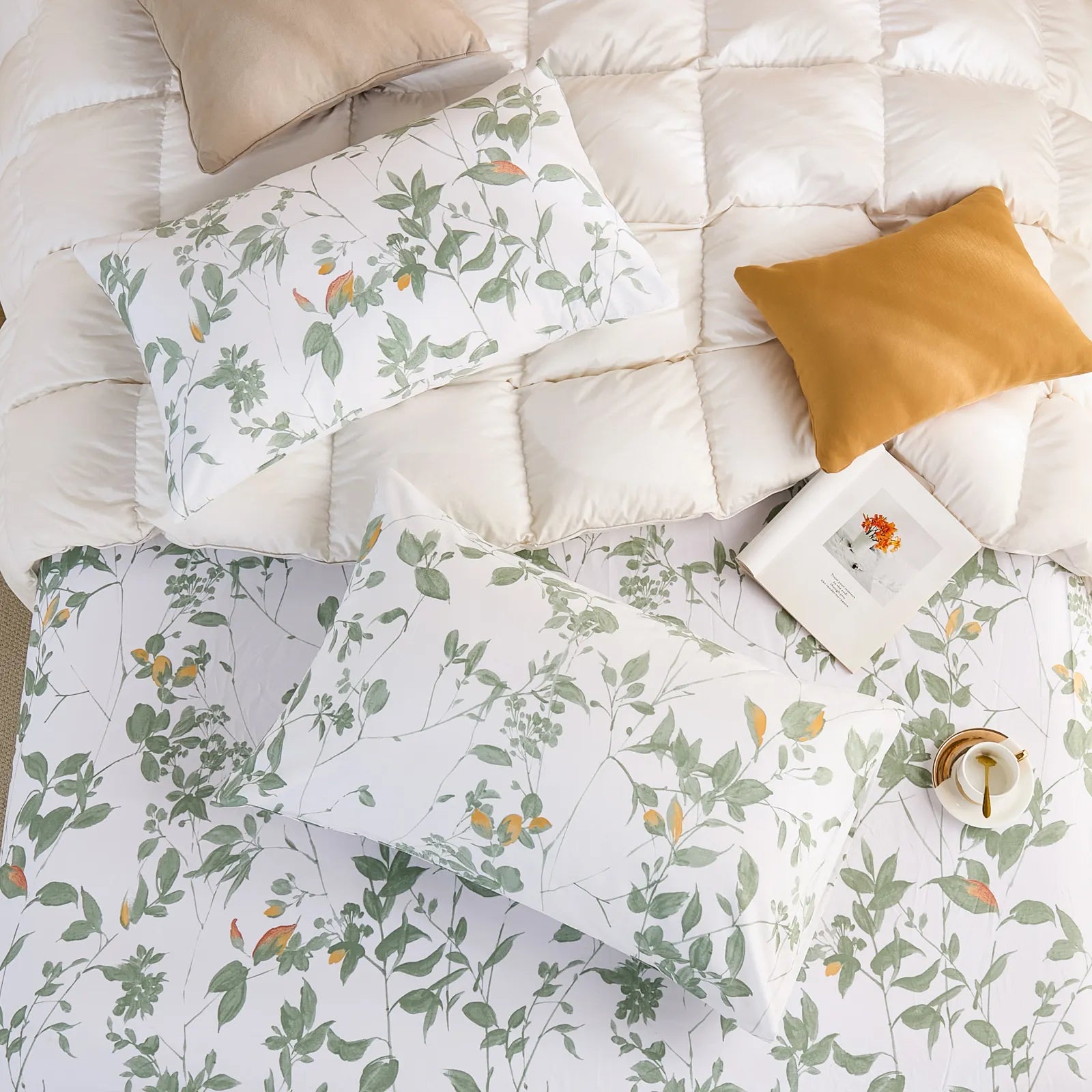 Overhead view of two cotton pillowcases and a fitted sheet with the green botanical print on a white duvet.