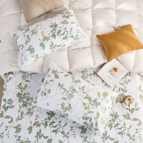 Overhead view of two cotton pillowcases and a fitted sheet with the green botanical print on a white duvet.