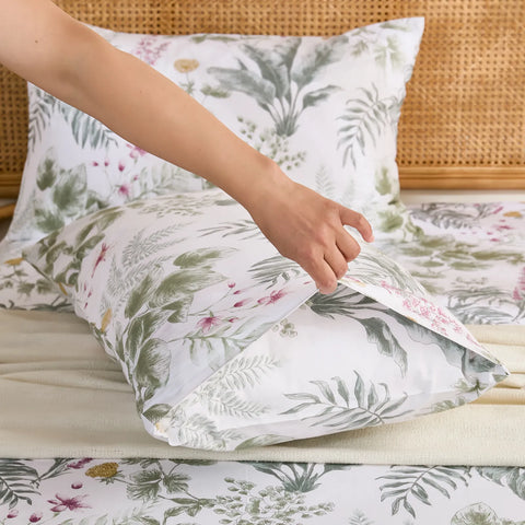 A hand tucking a pillow into the cotton pillowcase, showing the envelope closure detail and the dense leaf pattern.