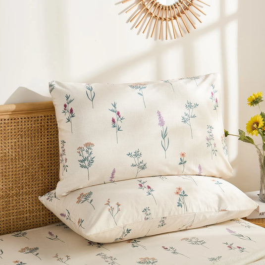 Close-up shot of two cotton pillowcases featuring a delicate, colorful wildflower and herb pattern, one propped up.