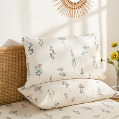 Close-up shot of two cotton pillowcases featuring a delicate, colorful wildflower and herb pattern, one propped up.