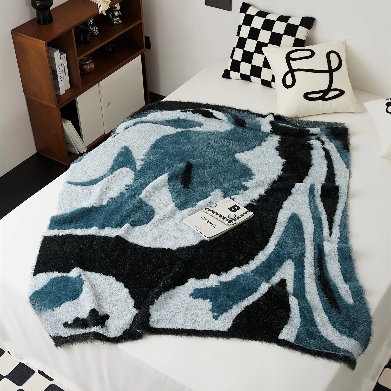 Abstract fuzzy knit throw blanket in teal and charcoal spread on white bed top down view