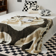 Large abstract fuzzy throw blanket in warm taupe and mocha spread over white bed in bedroom