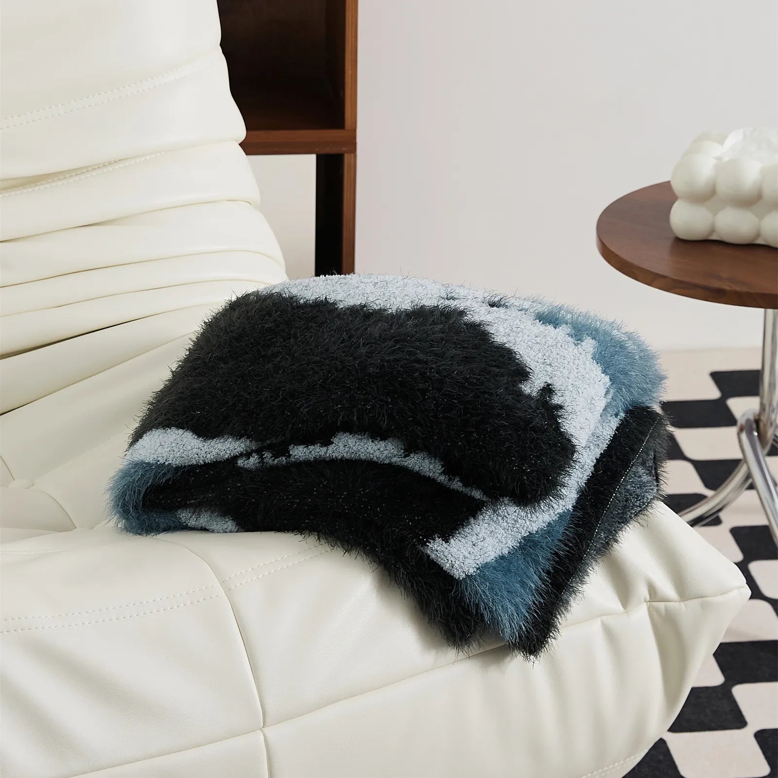 Abstract teal and black fuzzy blanket folded on white sofa armrest lifestyle shot