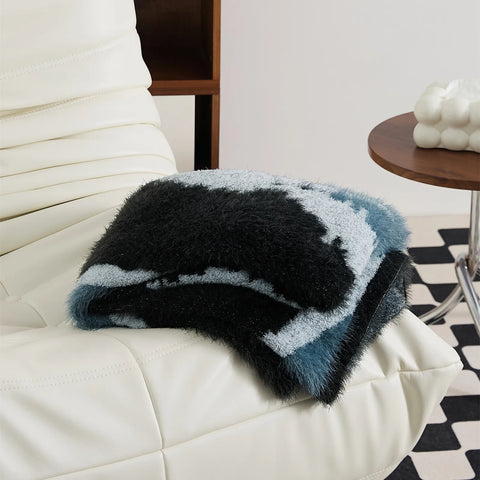 Abstract teal and black fuzzy blanket folded on white sofa armrest lifestyle shot