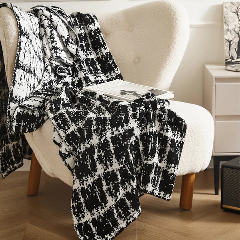 A cozy, artistic black and white wool blanket draped over a modern armchair, adding a touch of style to a living room.