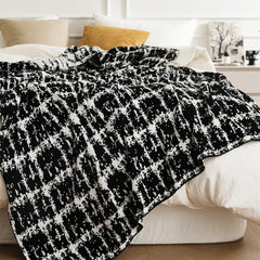 The black and white artistic wool blanket styled as a throw on a white bed, creating a chic and comfortable look.