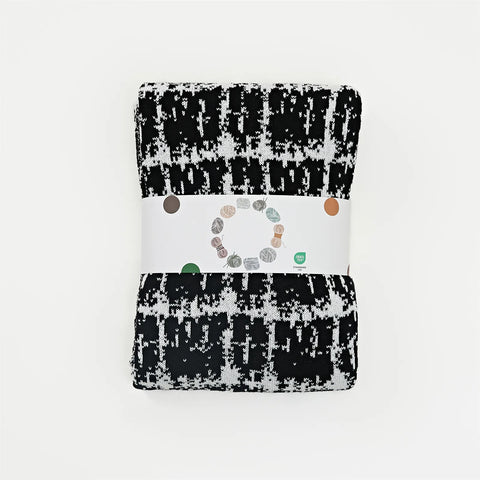 A neatly folded and packaged artistic black and white wool blanket, ready for retail.