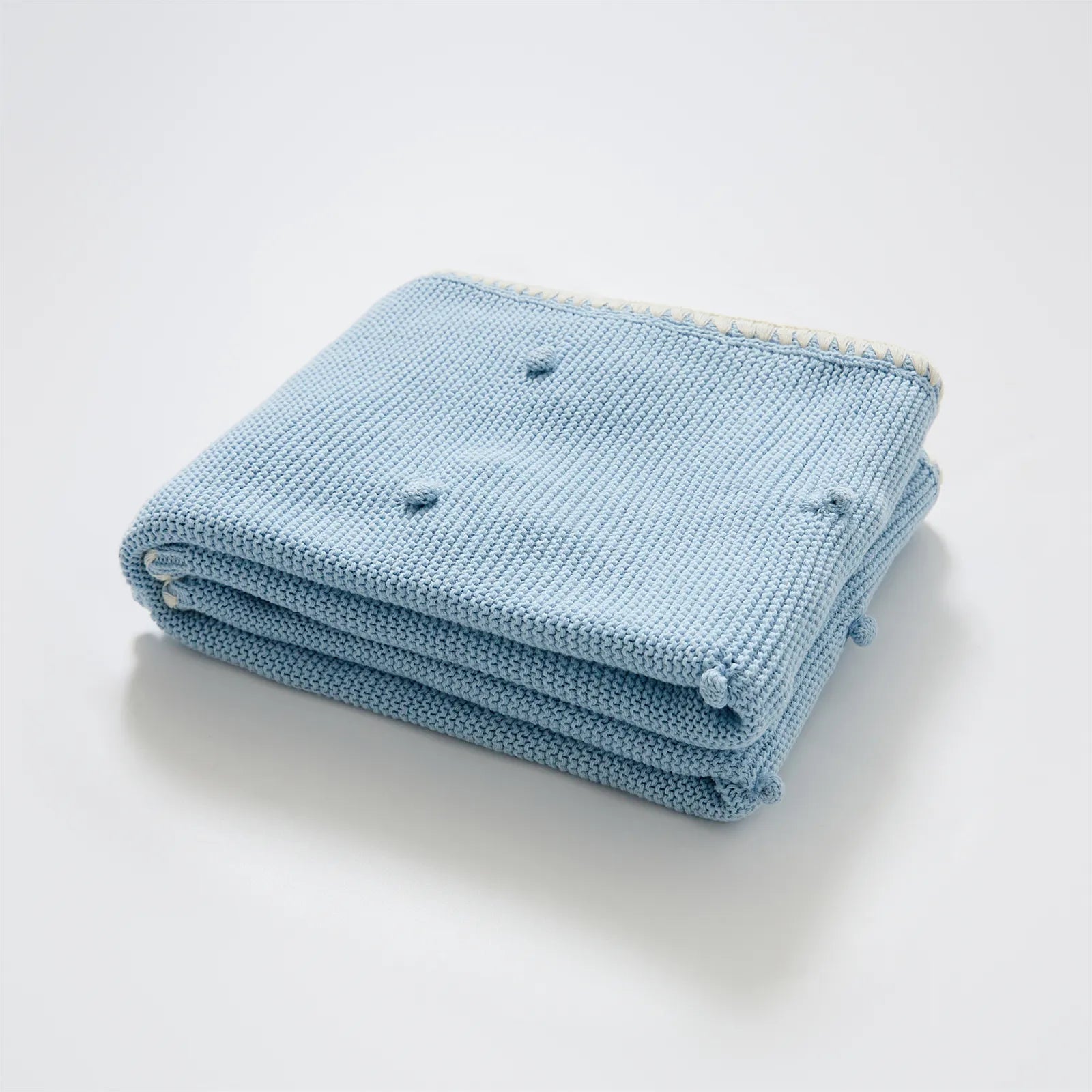 Neatly folded baby blue cotton knit throw blanket with cream fringe trim and bobble texture
