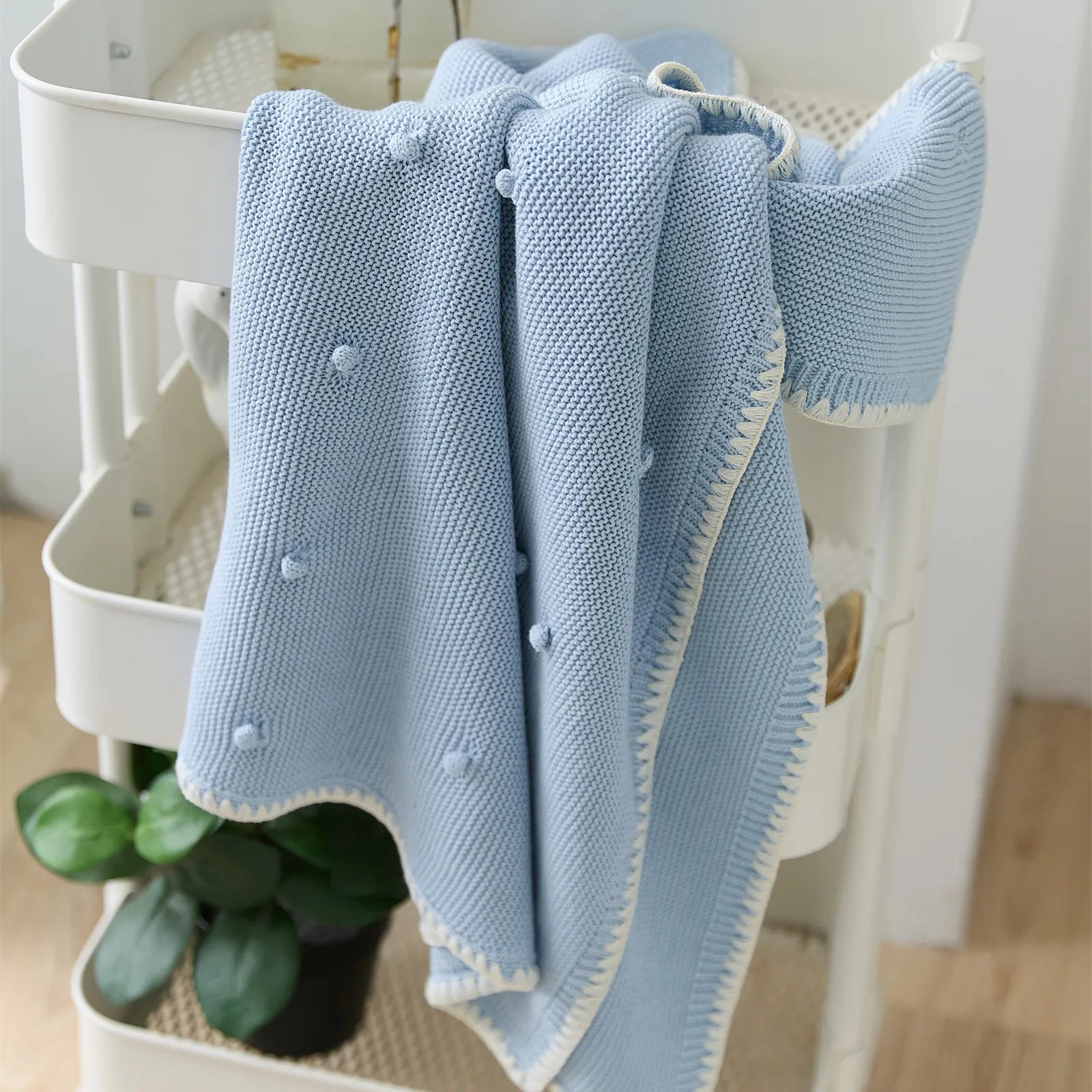 Baby blue cotton bobble throw draped over a white rolling cart with a green houseplant