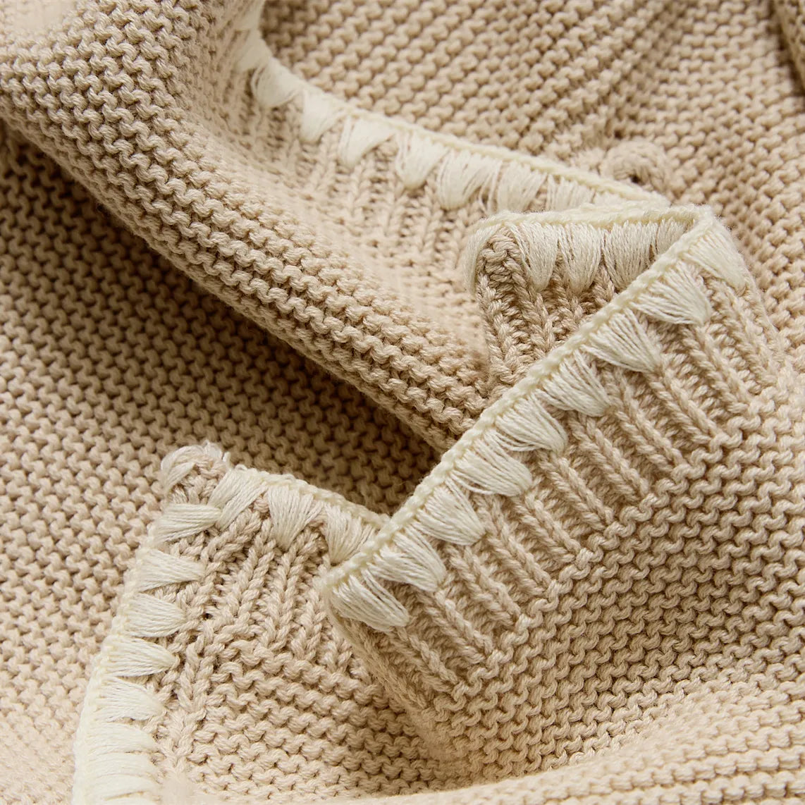 Close up detail of beige cotton knit showing the bobble texture and cream decorative fringe