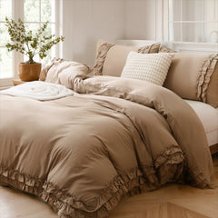 Beige cotton double ruffle duvet cover set with a grid-pattern pillow and a plant in a terracotta pot.
