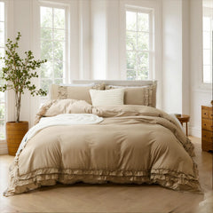 Beige cotton ruffle bedding set on a bed with matching pillows, next to a green plant in a wooden planter.