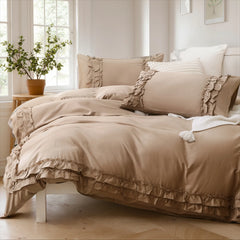 Beige cotton ruffle duvet cover and shams in natural light, with a white knit blanket at the foot of the bed.