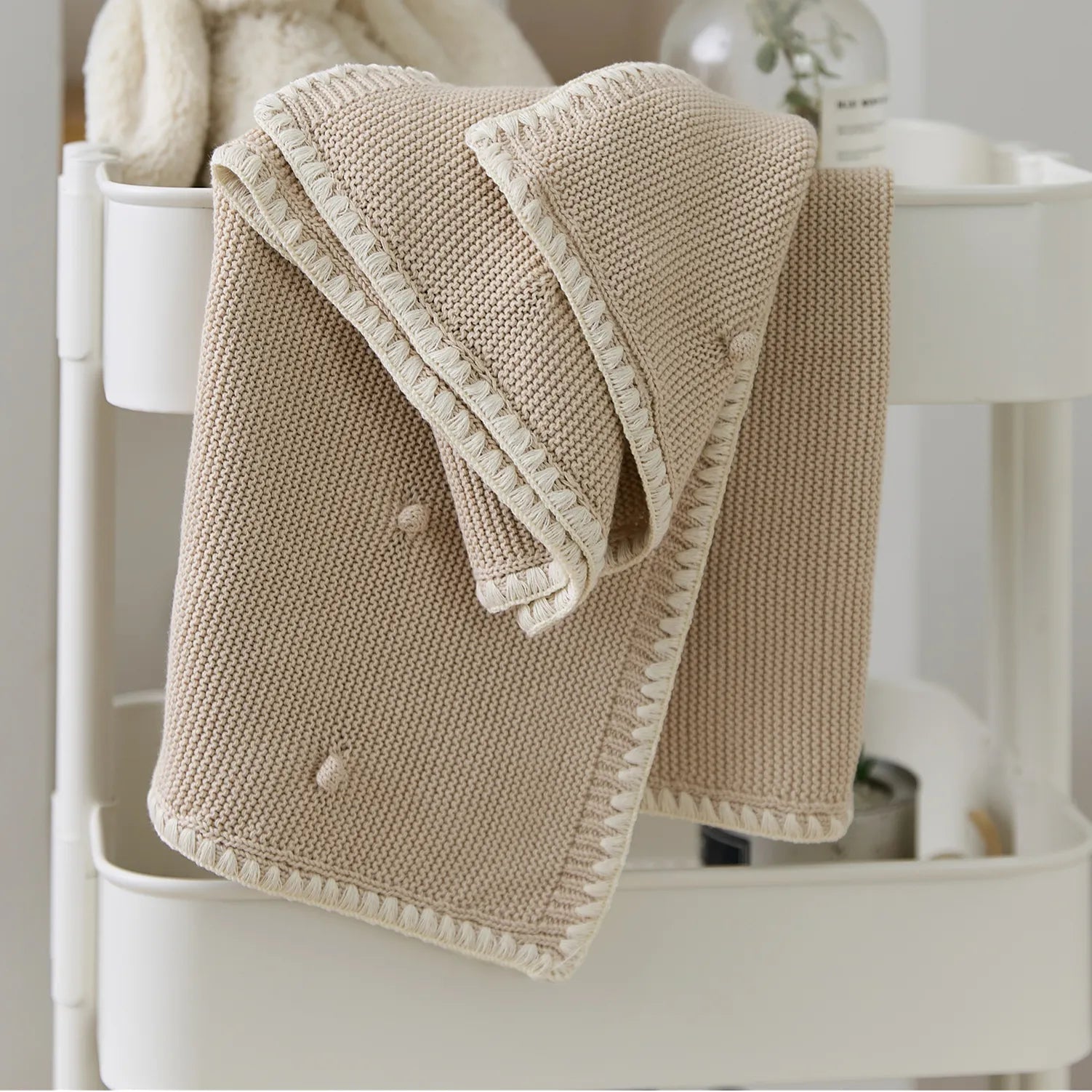 Folded beige cotton bobble throw placed on a white storage cart with a white rabbit toy