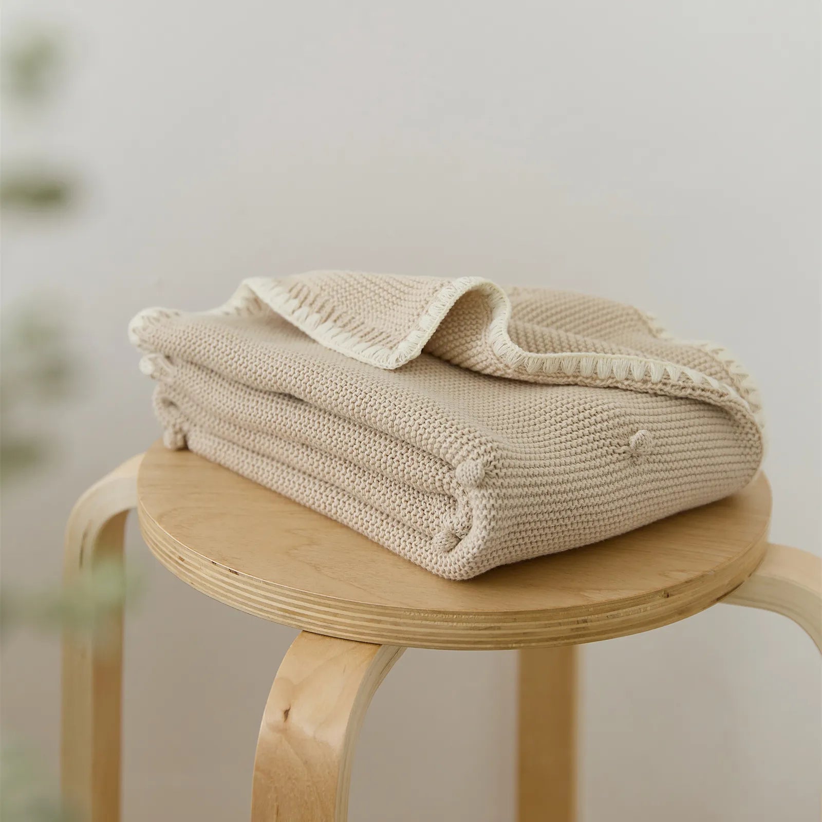 Folded beige cotton bobble throw placed on a wooden stool in a minimal setting