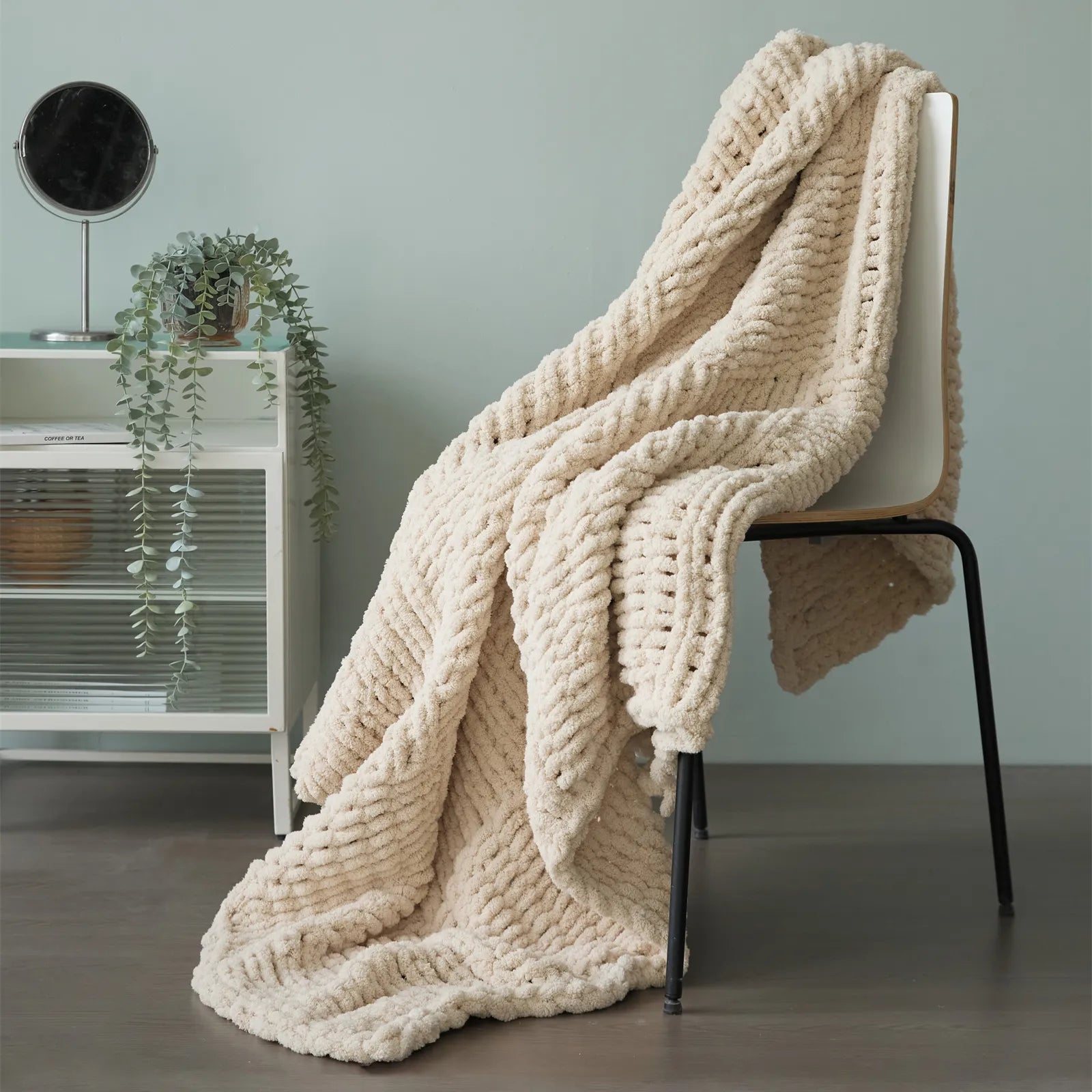 A plush beige chunky knit blanket is elegantly draped over a chair, perfect for adding a layer of warmth and style