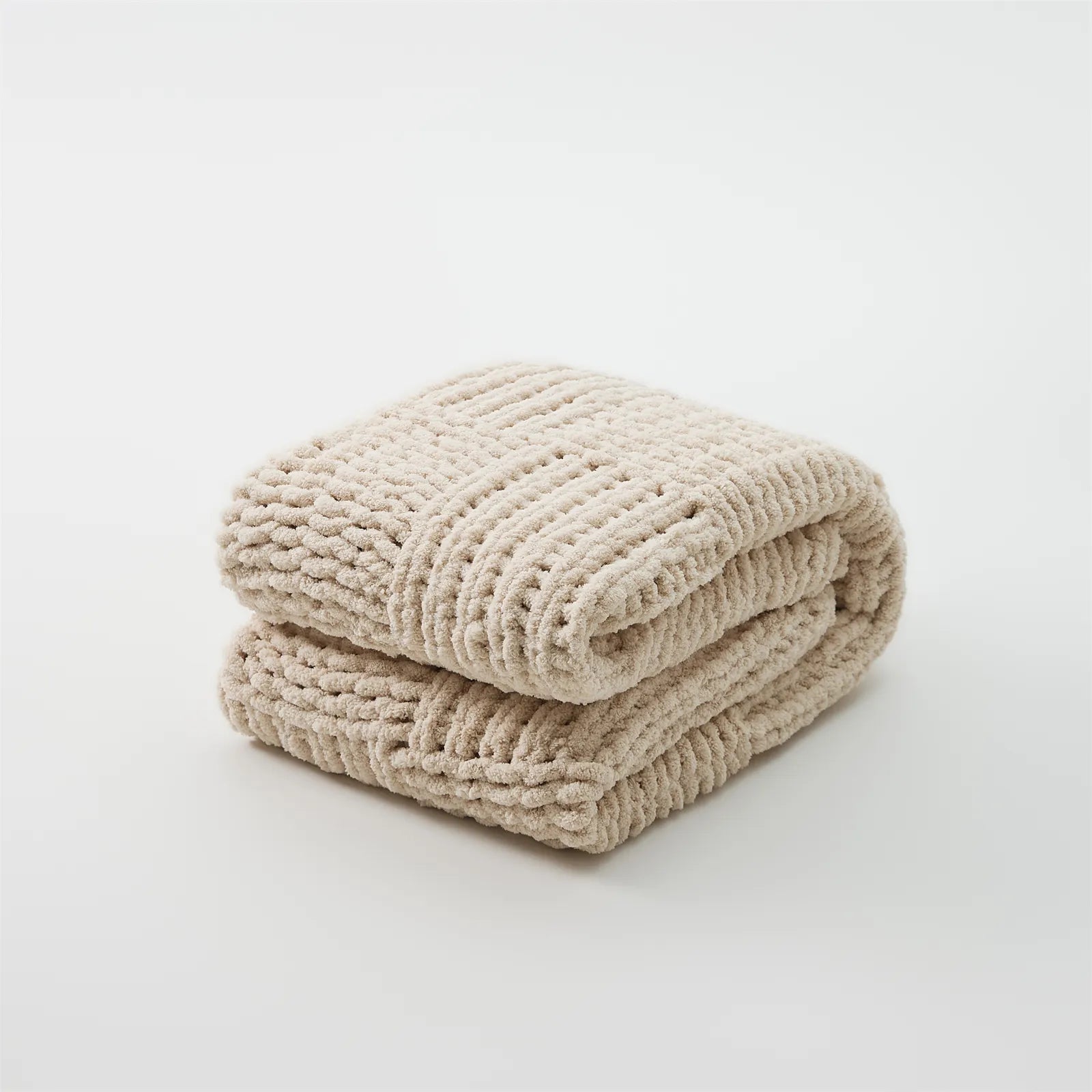 A studio shot of a perfectly folded beige chunky knit blanket, highlighting its neat texture and soft color