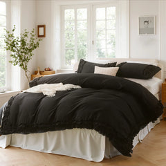 Black cotton double ruffle duvet cover on a bed with a white pillow, under botanical wall art and three windows.