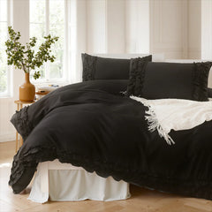 Black cotton double ruffle duvet cover on a white bed by a window with a green plant and natural light.