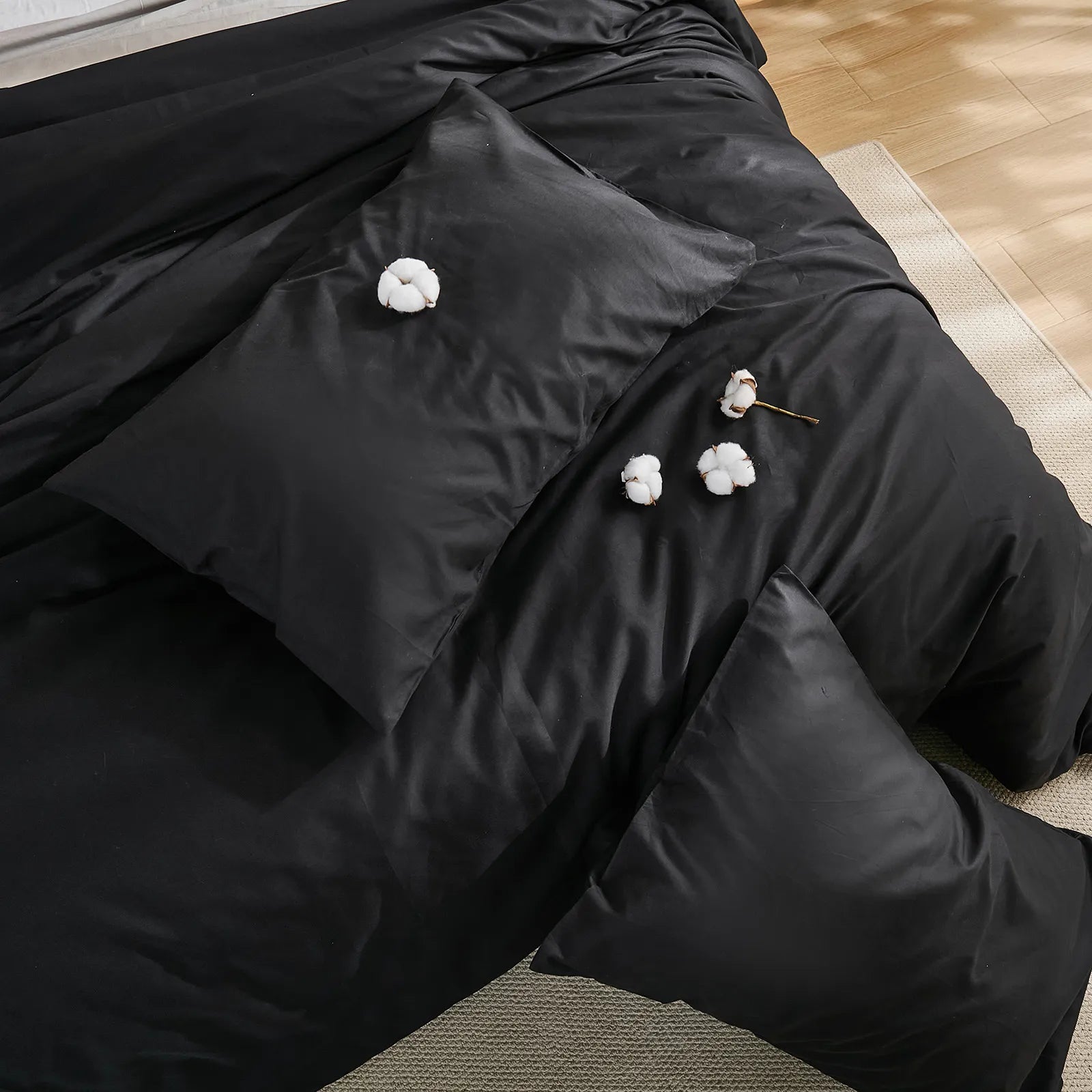 Top view of black solid duvet with four cotton blooms arranged on surface