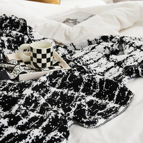 A detailed view of the artistic black and white wool blanket on a bed, with a matching checkered mug for a coordinated aesthetic.