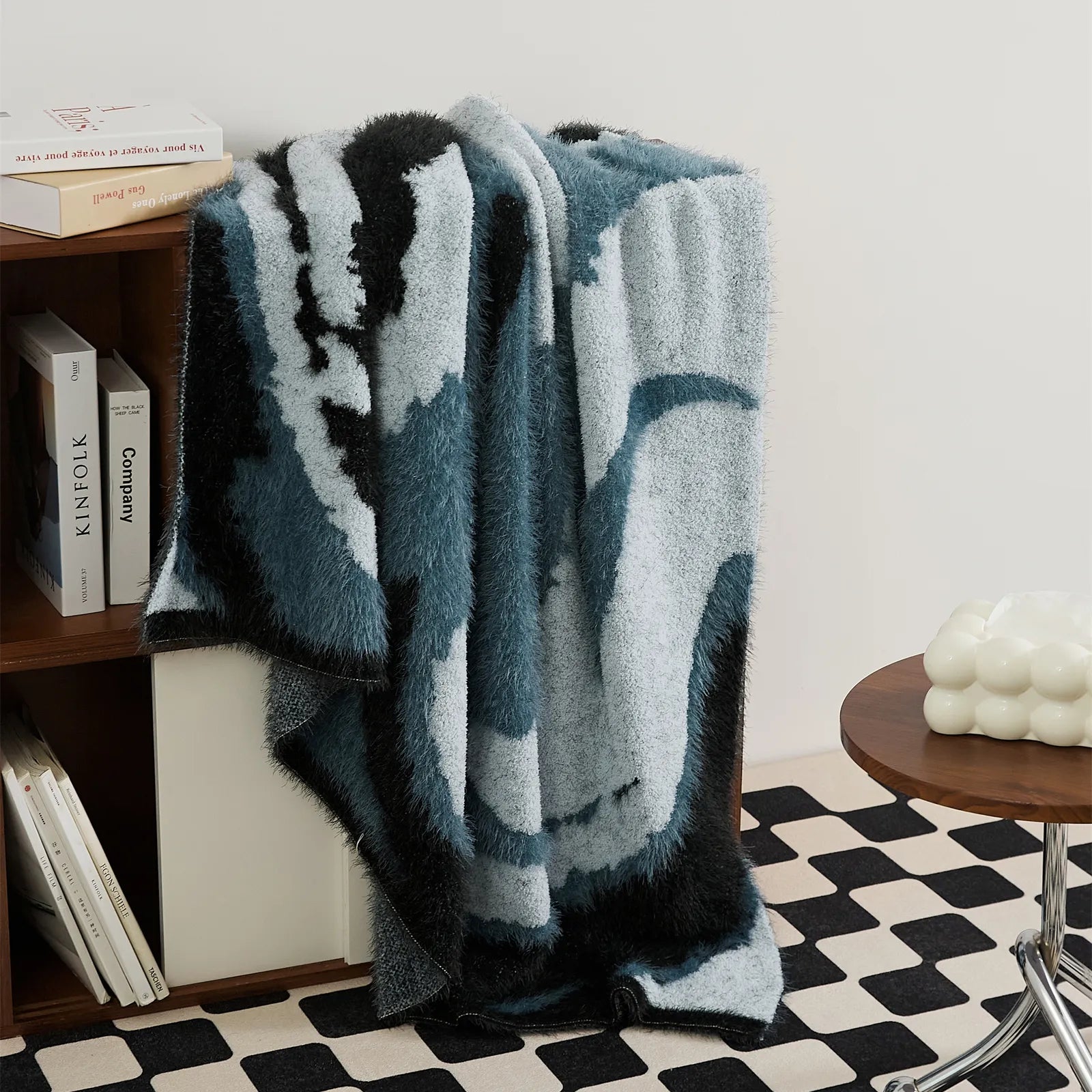 Long drape of teal denim fuzzy throw blanket displayed on dark wood storage shelf