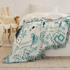 A cozy Prussian blue bohemian blanket styled as a throw on a bed with a matching decorative pillow.