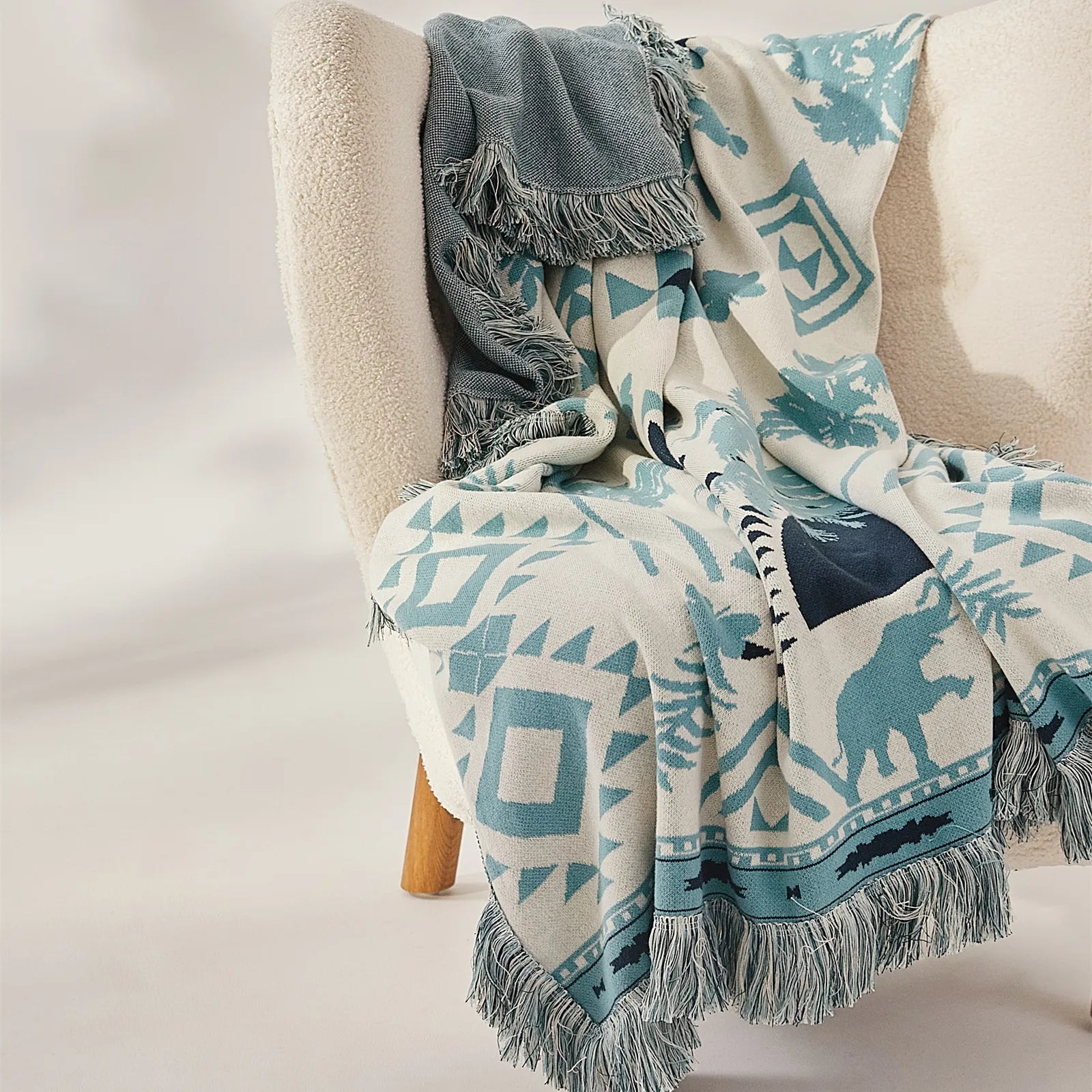 A Prussian blue bohemian tassel blanket draped over a light-colored couch, adding a pop of color and texture.