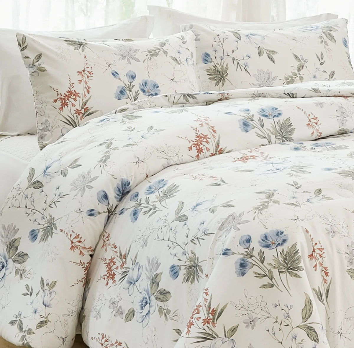 Close-up, corner view of a bed with a white comforter and pillows featuring a blue and orange floral pattern.