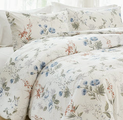 Close-up, corner view of a bed with a white comforter and pillows featuring a blue and orange floral pattern.