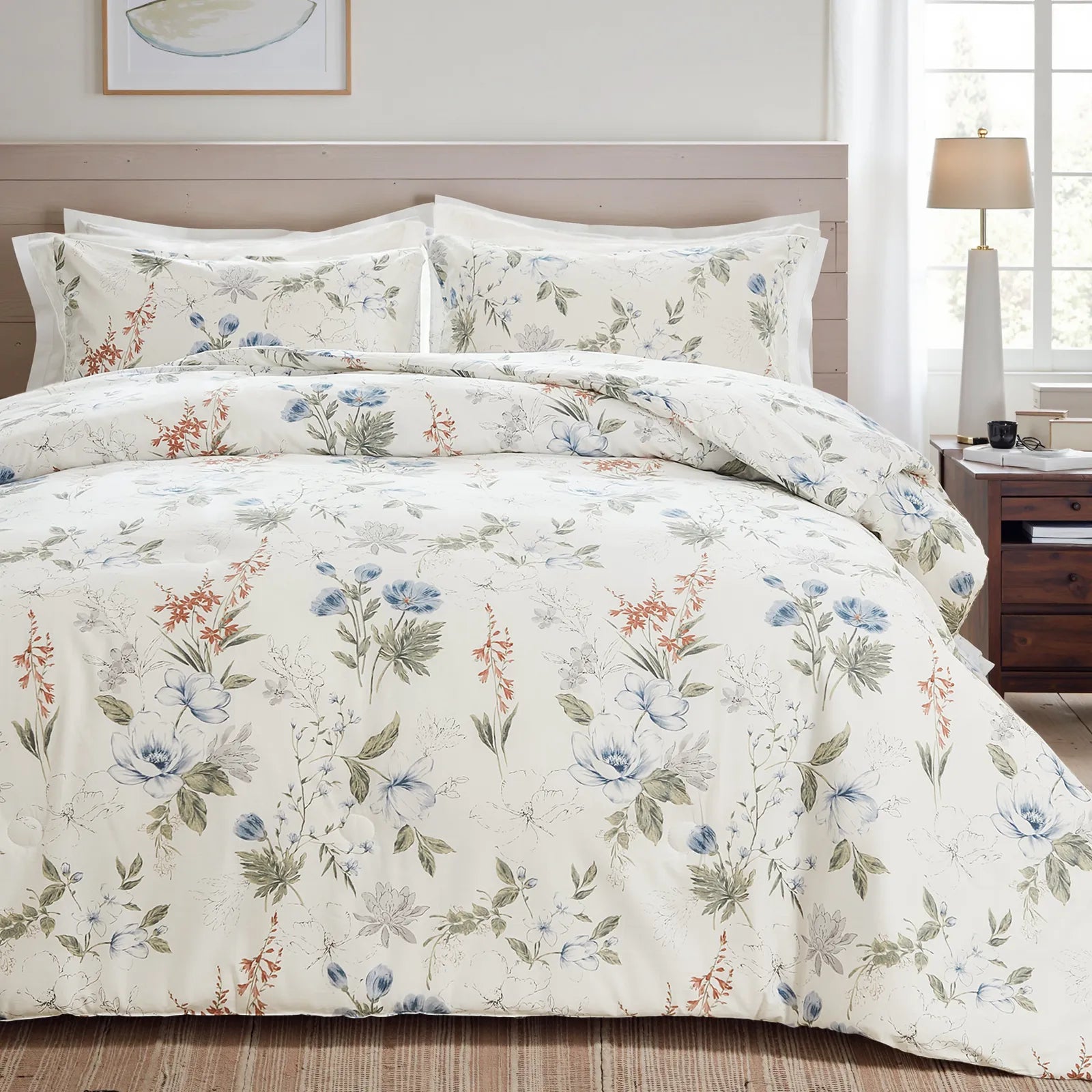 Full shot of a bed with a white floral comforter set, wood headboard, and a lamp on the nightstand.