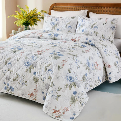  Angled view of a bed with a white and blue floral quilt, revealing the full pattern and texture.