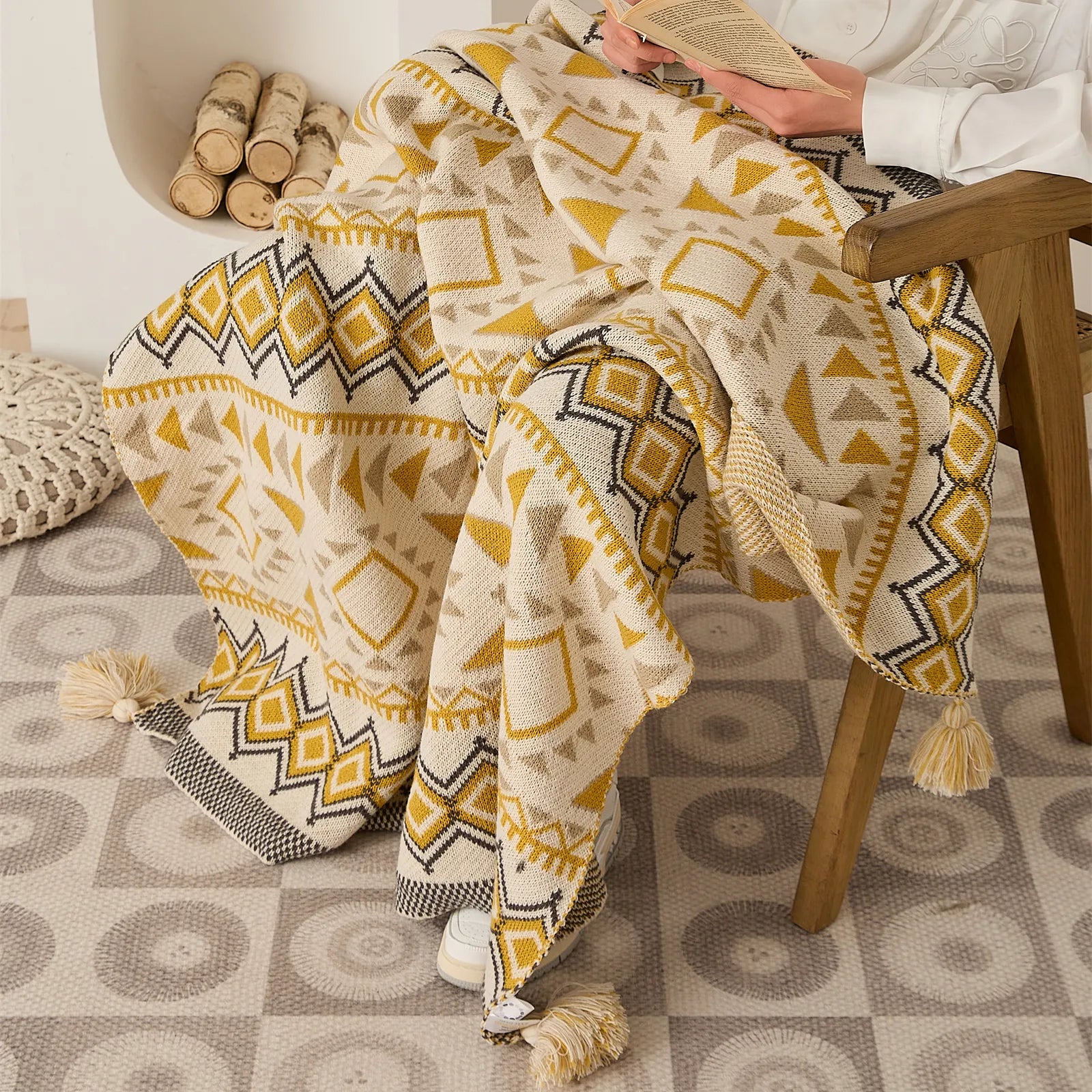Person reading with mustard yellow boho knit throw blanket draped on wooden accent chair