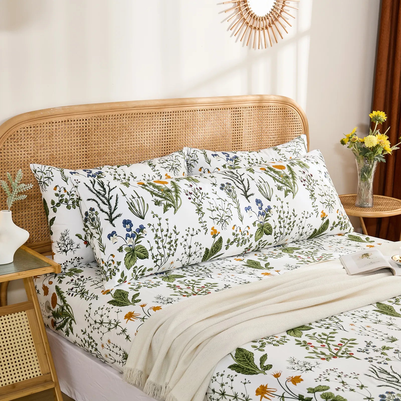 Three white cotton pillows, two standard and one long, displaying a botanical floral print on a beautifully made bed.