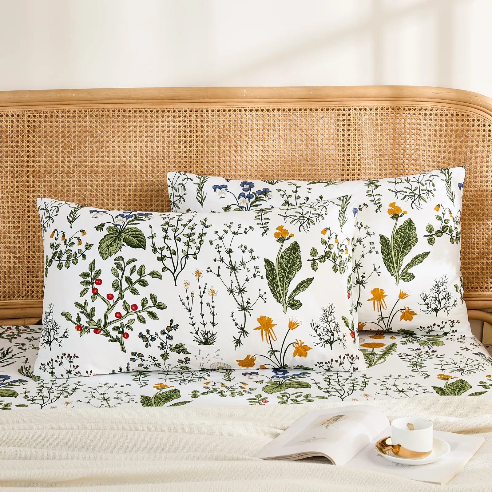 A pair of white cotton botanical print pillowcases featuring various colorful flowers and plants, neatly placed on a bed with a woven headboard.
