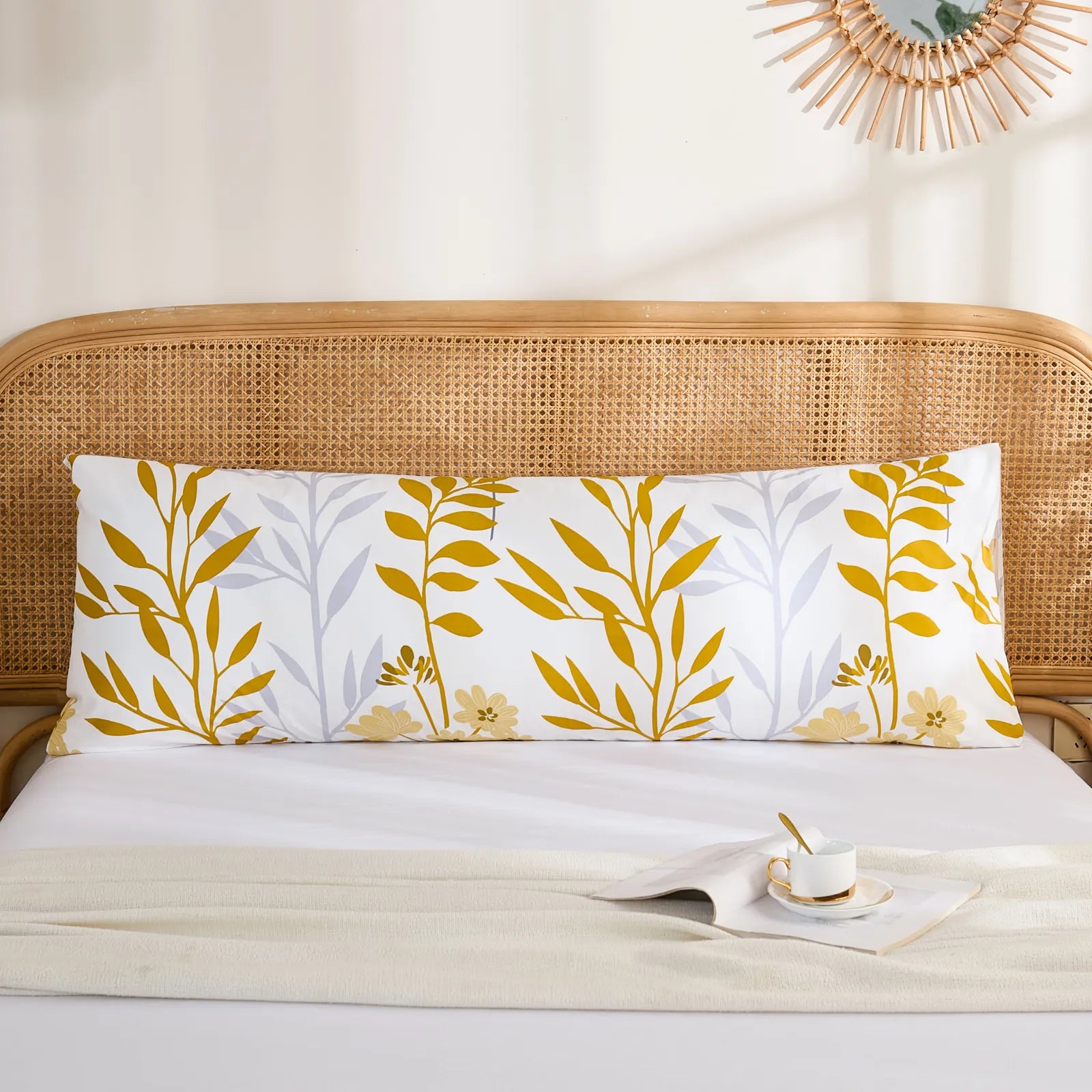 A long white cotton body pillow with a yellow leaf and grey floral print on a bed, styled in a cozy bedroom setting.