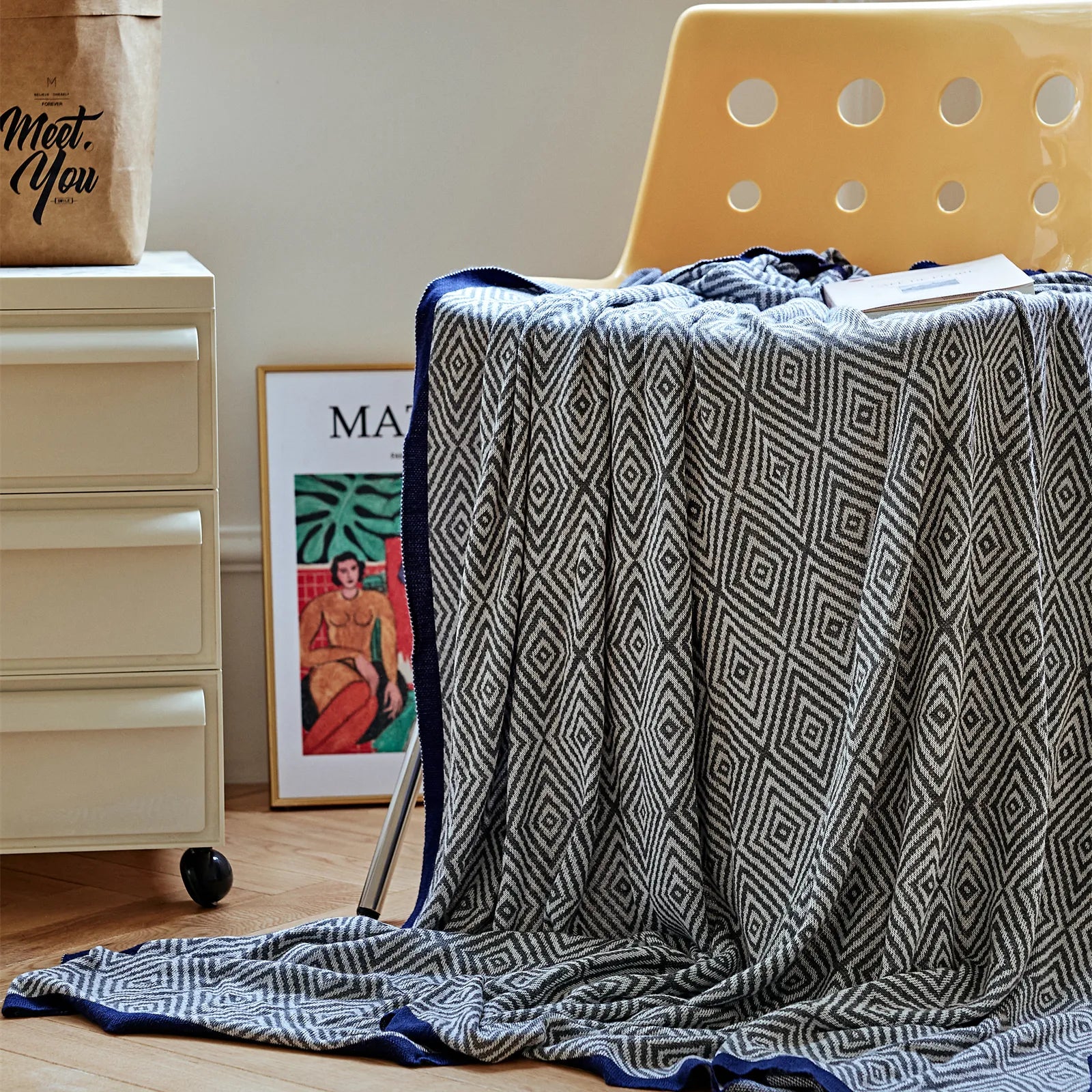 Charcoal-grey diamond pattern throw with a navy-blue border draped over a modern yellow chair.