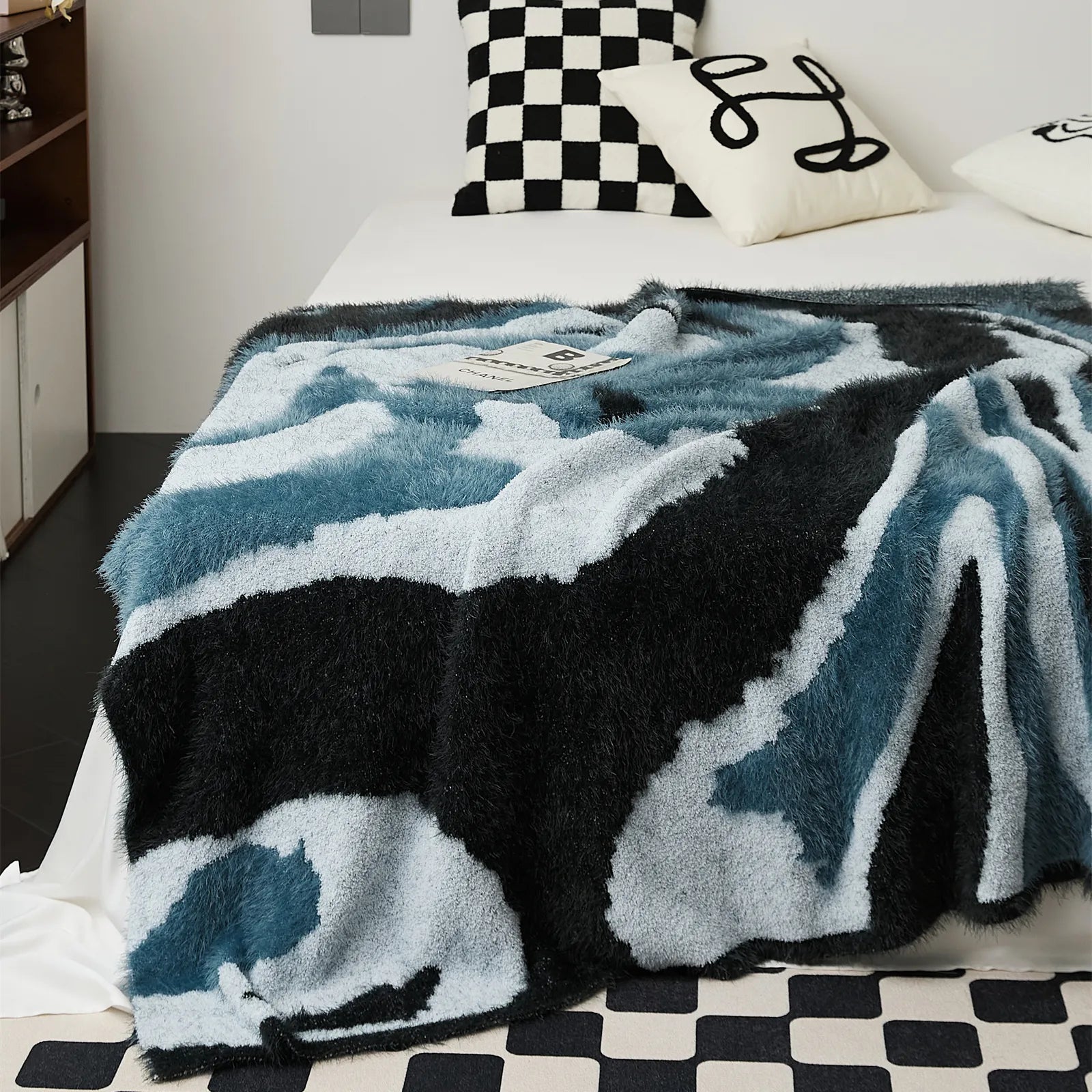 Close up detail of fuzzy knit blanket in denim blue and charcoal black on white bed